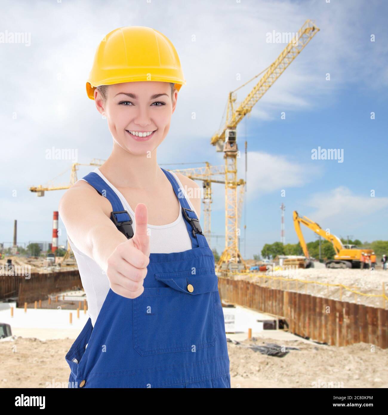 hermosa mujer constructor en overoles azules pulgares para arriba en sitio  de la construcción Fotografía de stock - Alamy