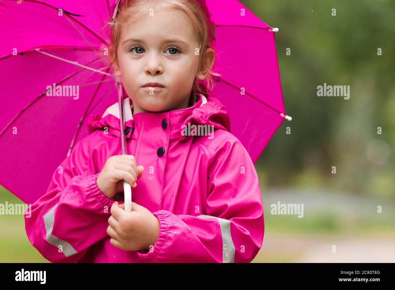 Lindo niño niña de 2-3 años de edad con un impermeable rosa con estilo que  sostiene paraguas en el parque sobre fondo verde naturaleza. Mirando la  cámara. Childhoo Fotografía de stock - Alamy