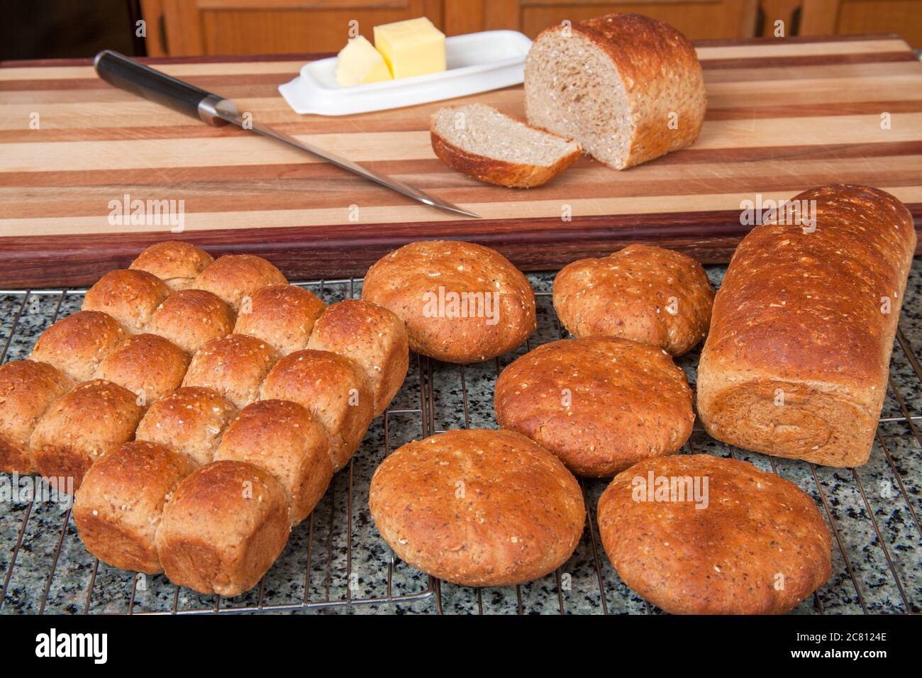 Multigrain panecillos, bollos y pan con un trozo cortado, con mantequilla y un cuchillo de pan. Foto de stock
