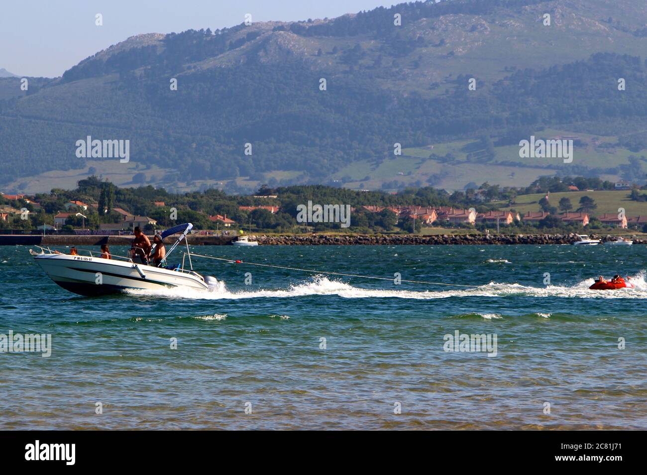 Velero de movimiento rápido remolcando gente en un anillo de goma naranja inflado en la bahía de Santander Foto de stock