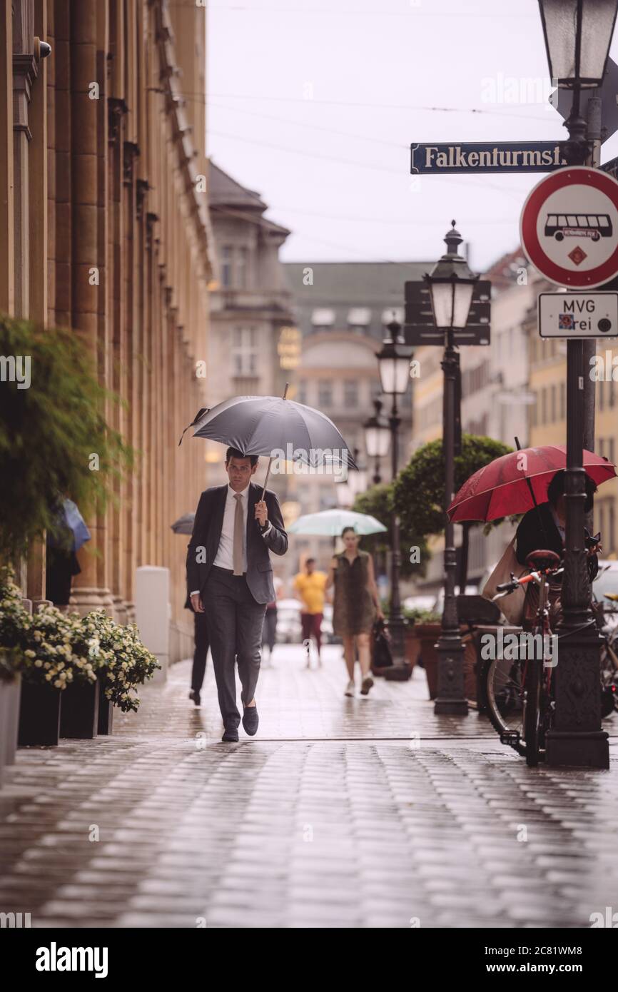 MUNICH, ALEMANIA - 07 de julio de 2020: Hombre de negocios en un traje en  la calle de la ciudad durante la lluvia. Hombre con sombrilla en el centro  de Munich Fotografía