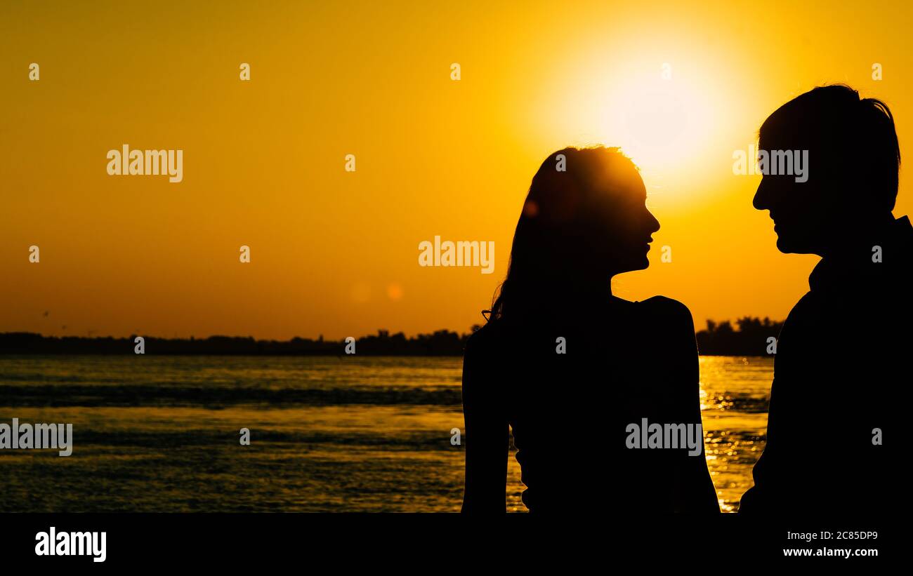 Pareja joven enamorada se encuentra con el amanecer (puesta de sol) en las orillas del río. Foto de stock