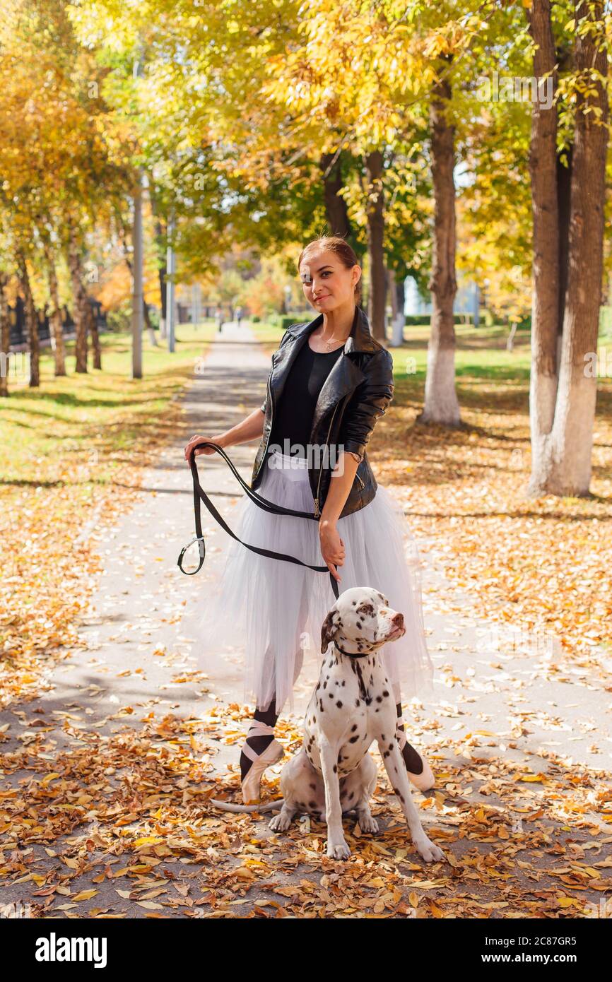 Bailarina con perro dálmata en el parque. Mujer bailarina de ballet en un  blanco de la falda y la chaqueta de cuero negro bailando en Pointe zapatos  en otoño parque con Fotografía