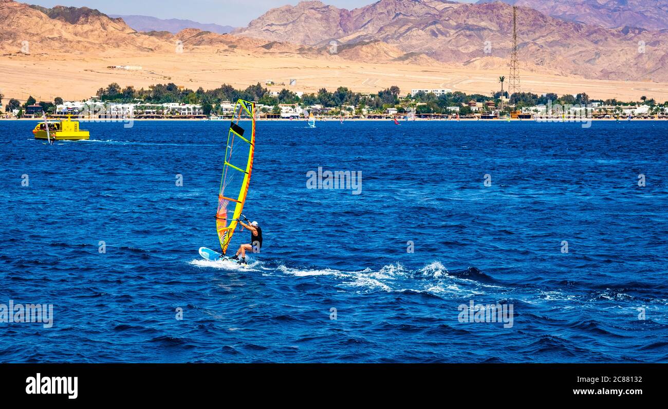 Hombre con deporte de windsurf extremo en el mar azul con playa de arena en el fondo Foto de stock