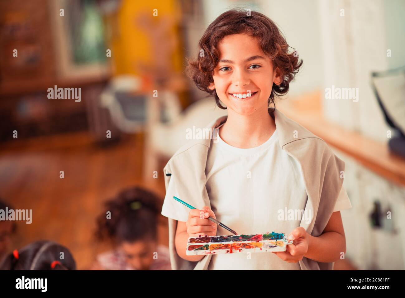 Niño sonriente sosteniendo una paleta de acuarelas Foto de stock