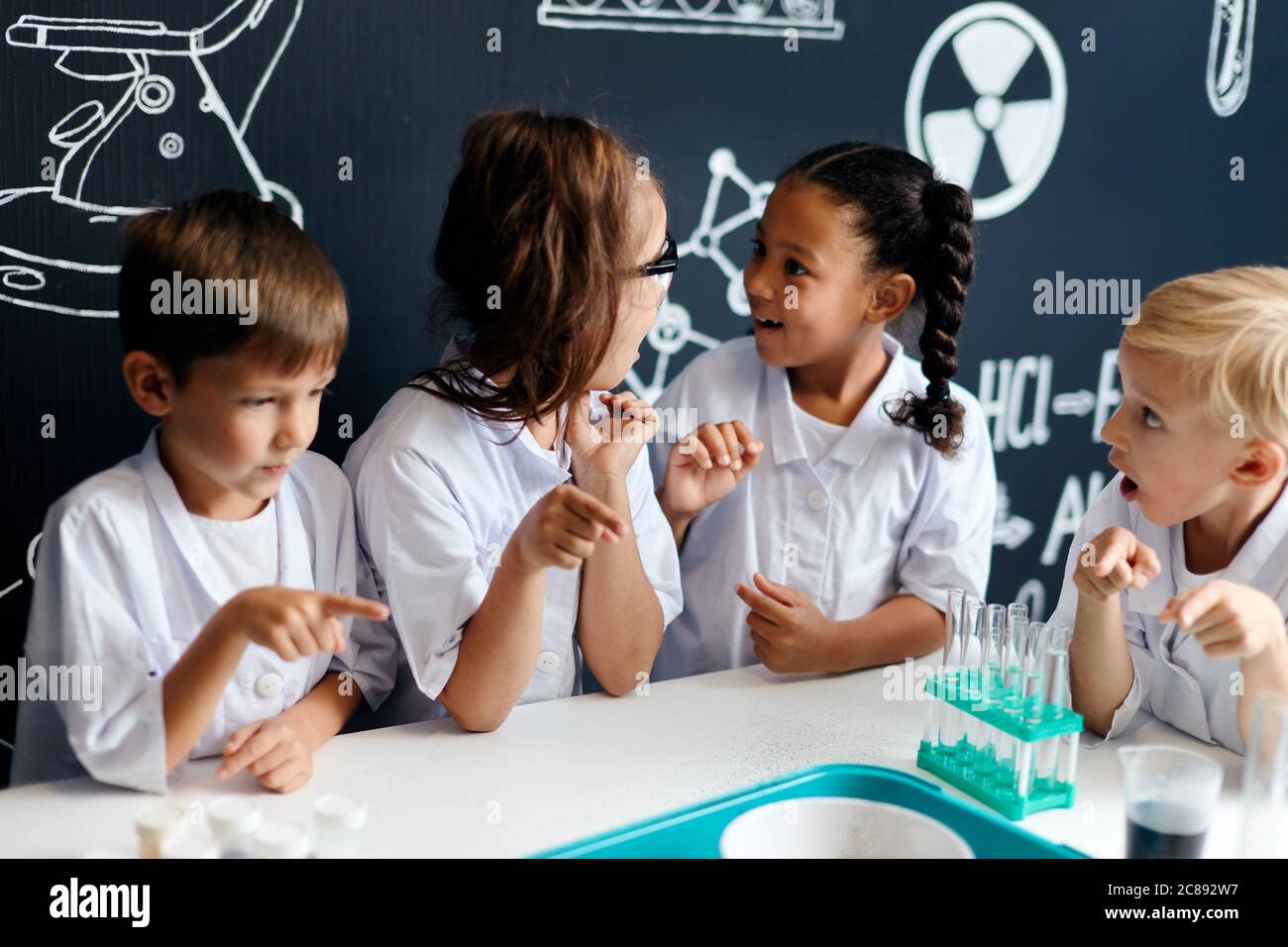 Grupo de niños multirraciales diversos en ropa blanca científica haciendo experimentos científicos con reactivos en el laboratorio, sorprendiéndose y asombrándose Foto de stock