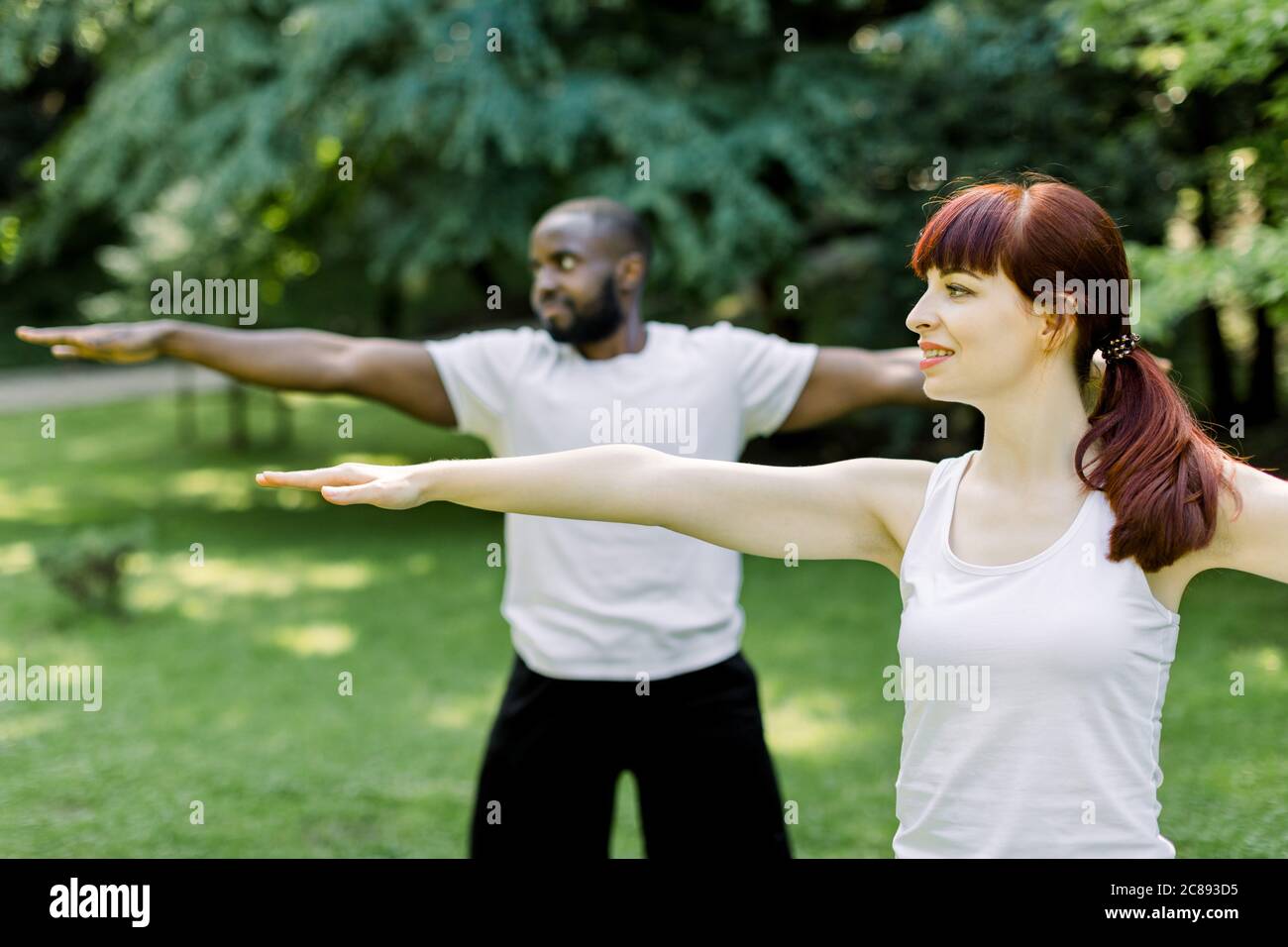 Concepto de un estilo de vida familiar saludable y yoga en el parque. Jóvenes parejas multiétnicas ejercitando al aire libre con los brazos estirados, mirando hacia adelante. Céntrese en Foto de stock