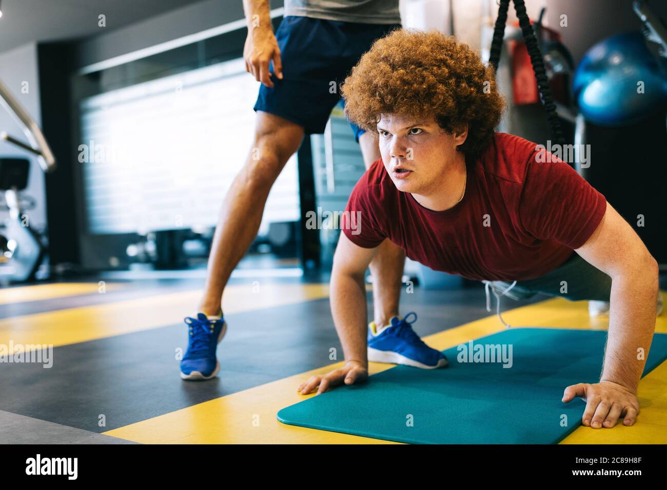 Fat a los hombres jóvenes con entrenador haciendo ejercicio en el gimnasio de fitness. Foto de stock