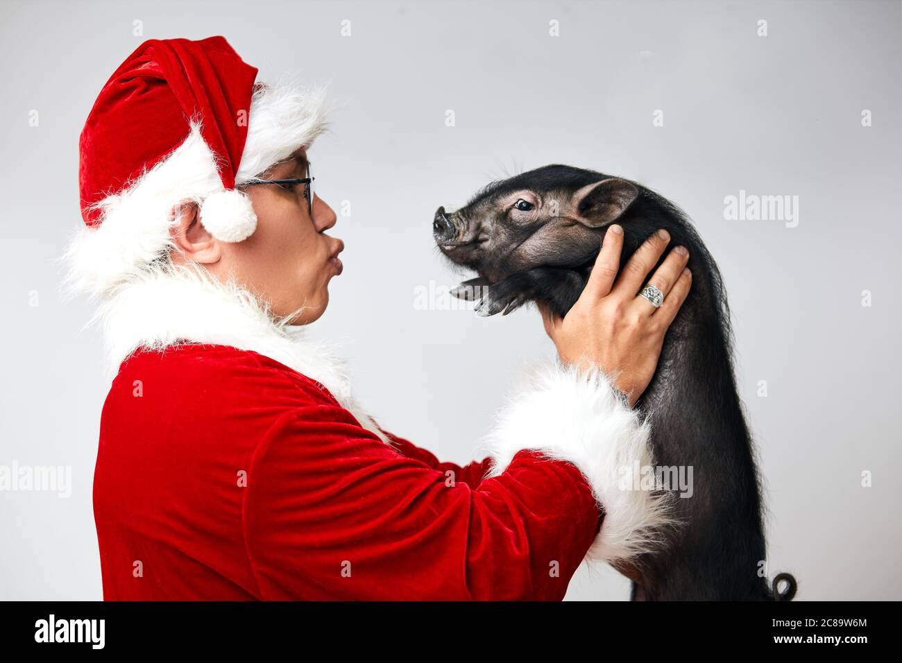 Perfil de la foto de Asia Santa Claus en traje de Navidad sosteniendo  pequeño negro mini cerdo planificación para besarlo, aislado sobre fondo  blanco con copyspace Fotografía de stock - Alamy