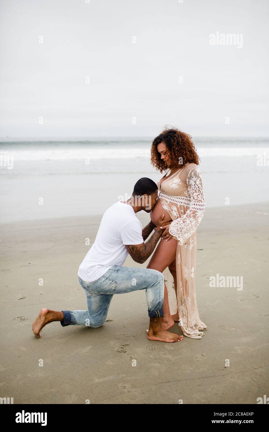 Pareja de carreras mixtas en la playa, besando a Baby Belly Foto de stock