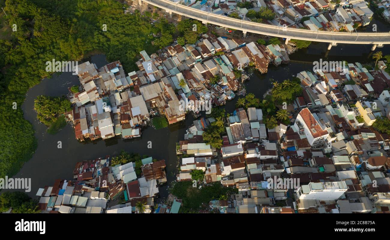 Antigua zona residencial y de negocios que se asemeja a una ciudad llena de gente de barrio, construida a lo largo de un canal desde la vista aérea de arriba abajo con el nuevo metro de Saigón Foto de stock