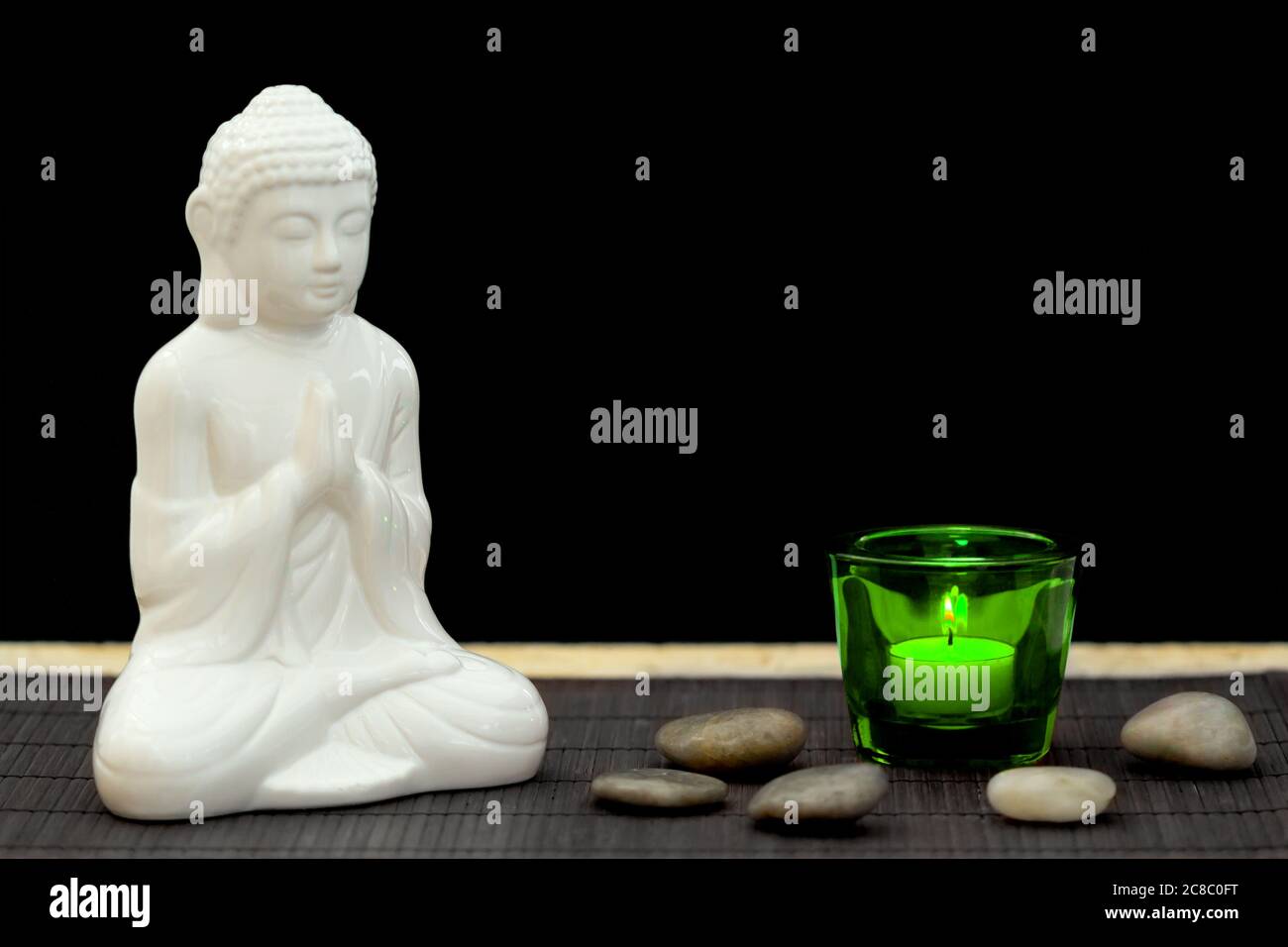 Figura blanca en meditación pose con guijarros y vela en un vaso verde desde el punto de vista Foto de stock