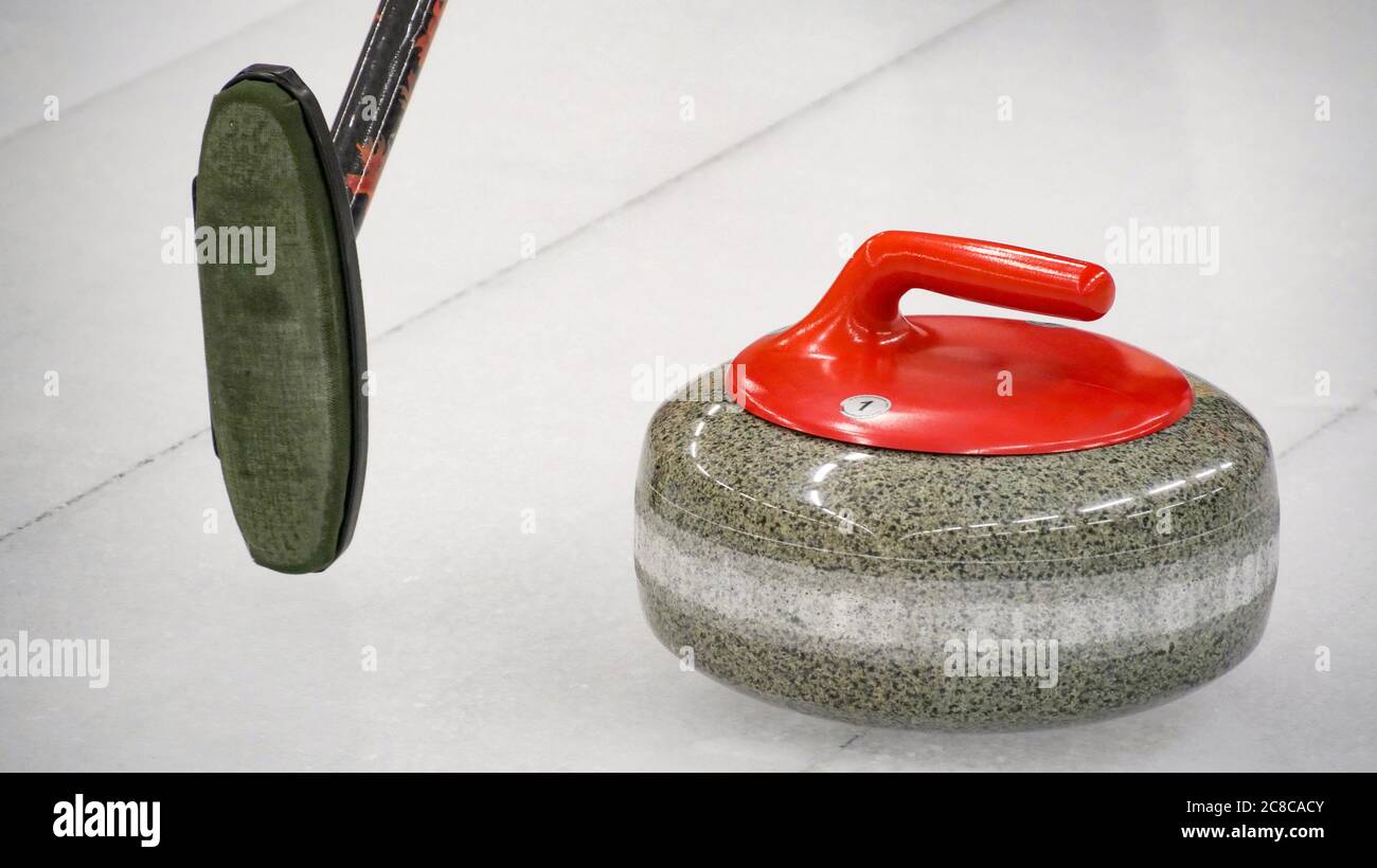 El juego de curling es un deporte olímpico de invierno. Piedra de rizado,  cepillo y plancha de rizado de hielo con círculo rojo y azul y guijarros  visibles Fotografía de stock -