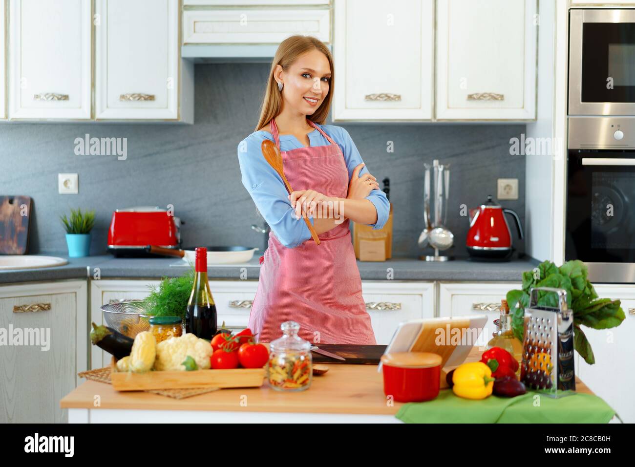Atractiva joven mujer en el delantal rojo de pie en su cocina Fotografía de  stock - Alamy