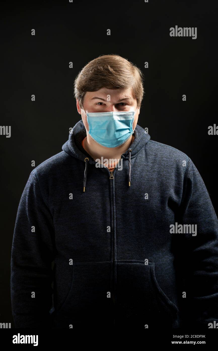 Hombre de 20 años con una máscara azul de tipo médico en un estudio. Máscara para detener la propagación del coronavirus covid-19 Foto de stock