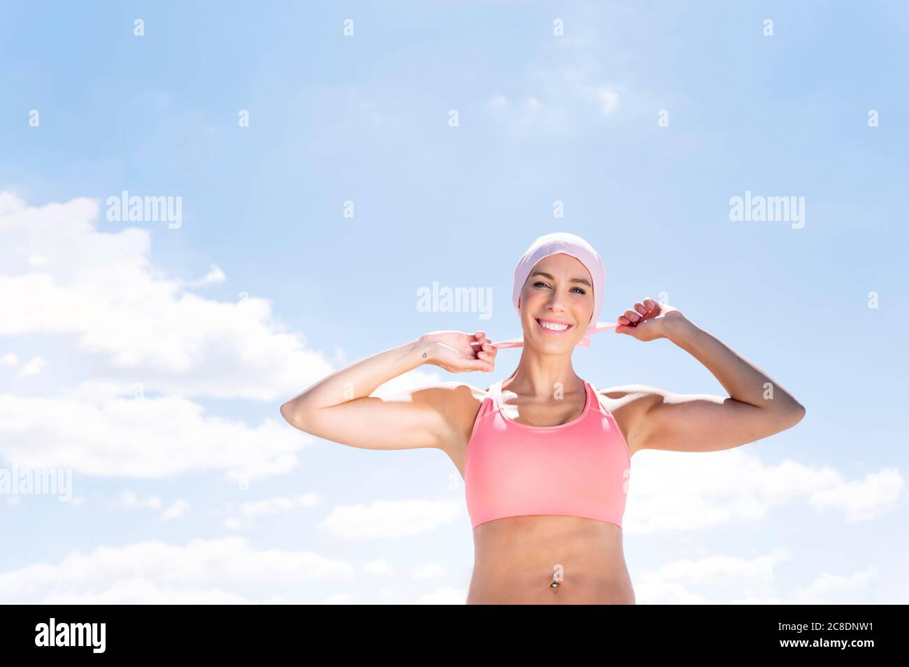 Feliz mujer deportiva con pañuelo mientras se está de pie contra el cielo azul Foto de stock