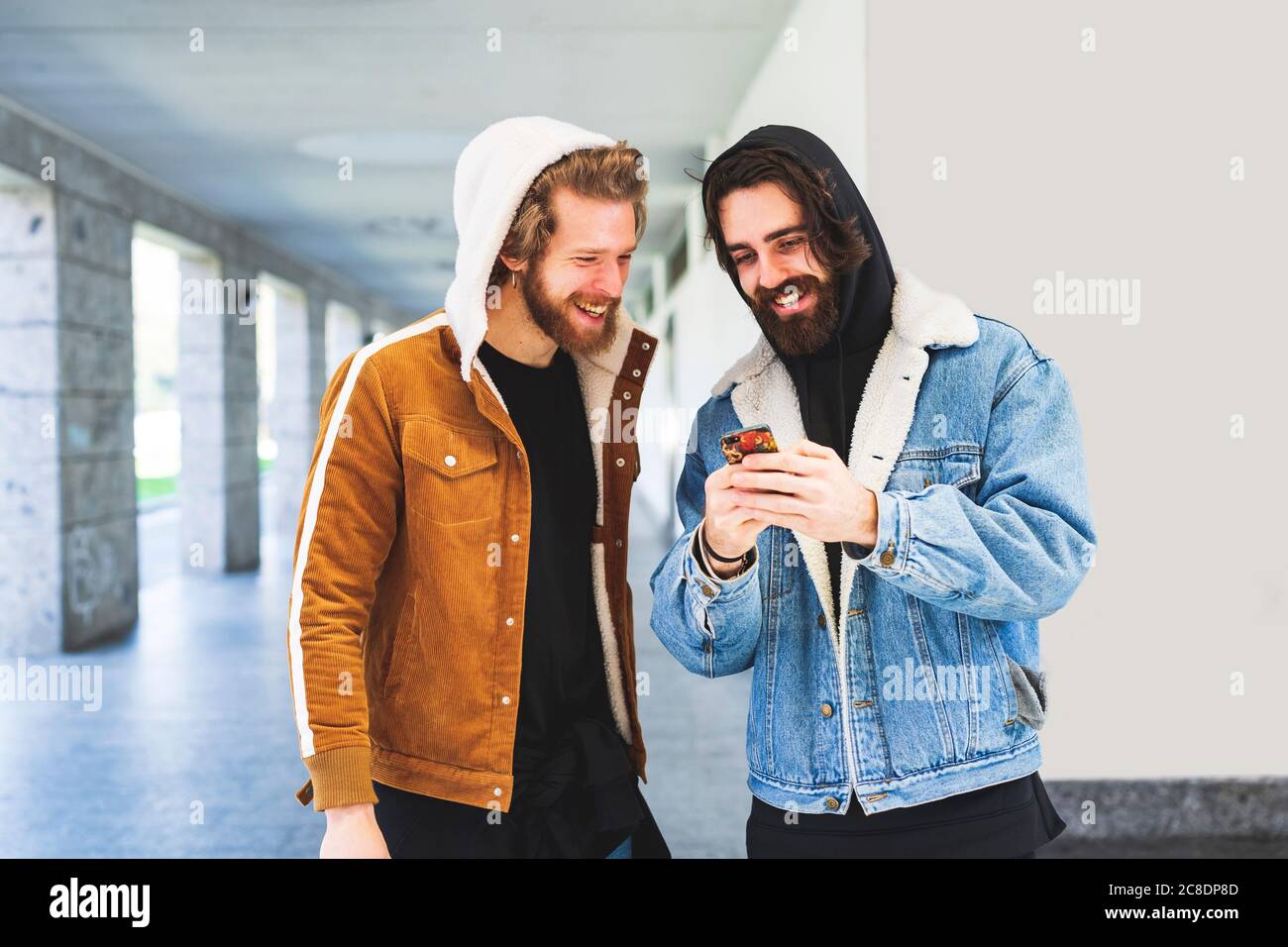 Hombre joven mostrando un teléfono inteligente a un amigo masculino mientras está de pie contra la pared Foto de stock