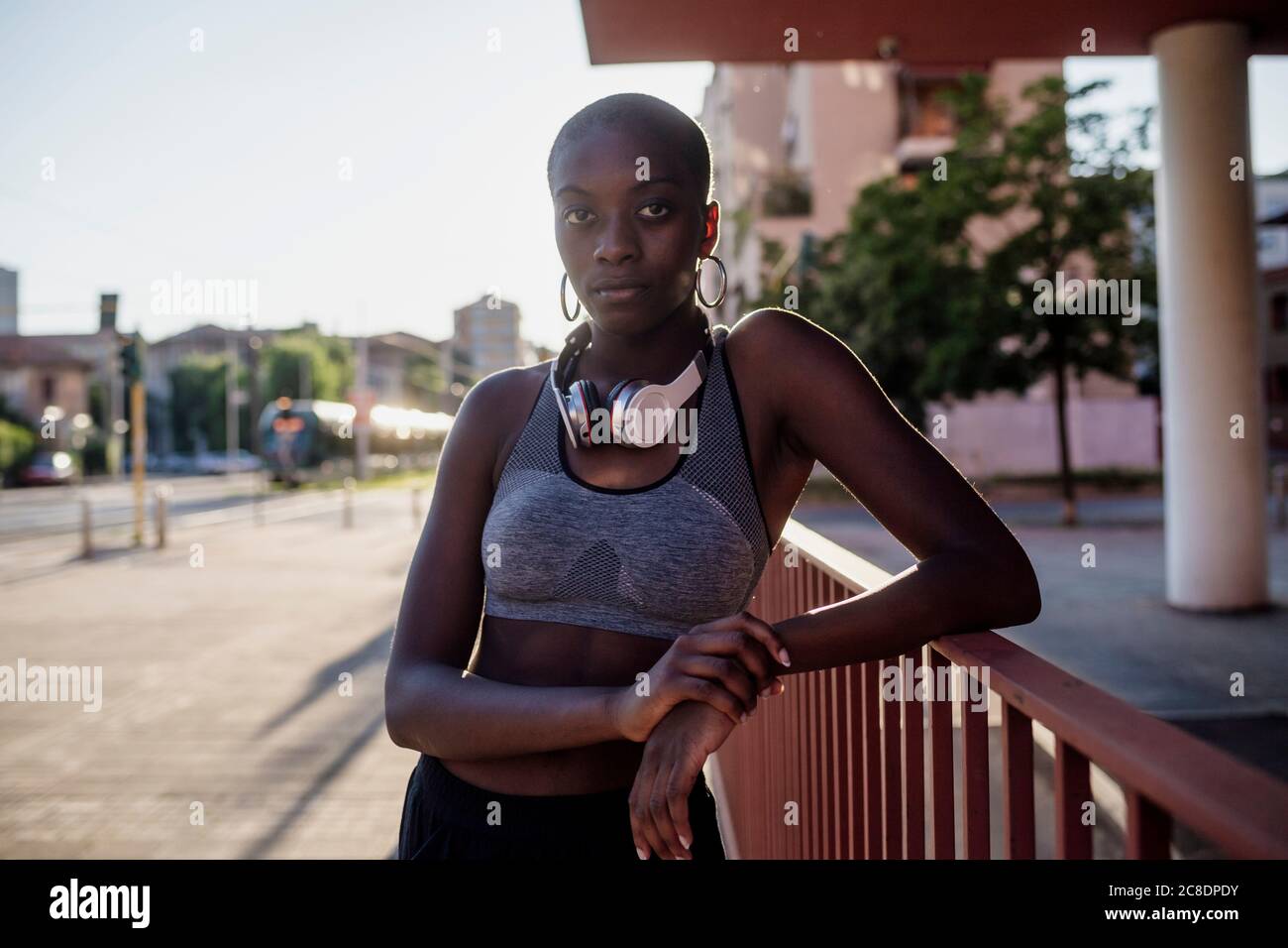 Mujer joven segura de sí misma con la cabeza afeitada de pie por la barandilla ciudad Foto de stock