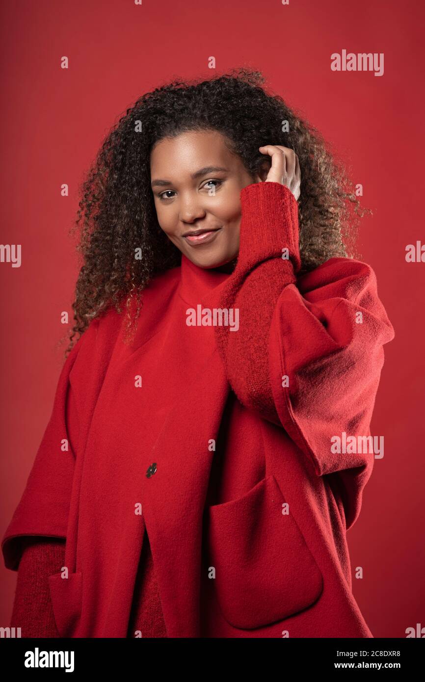 Mujer sonriente con pelo rizado usando abrigo mientras que está de pie  contra fondo rojo Fotografía de stock - Alamy