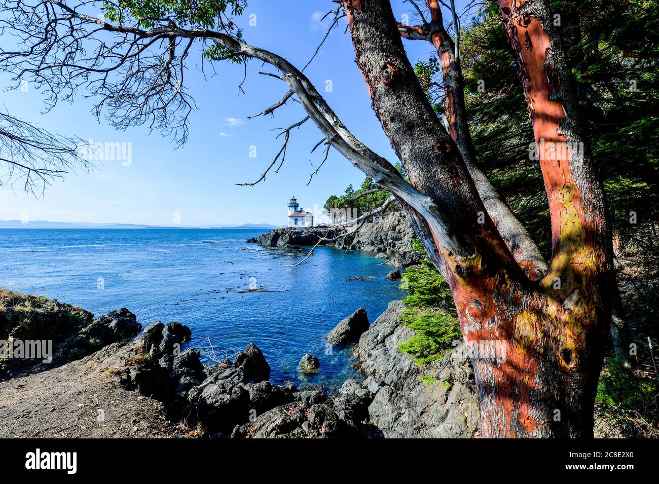 EE.UU., Washington, Isla de San Juan, costa rocosa con el faro de Lime Kiln en el fondo Foto de stock