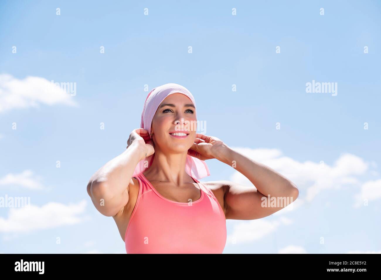 Una mujer deportiva pensativa que lleva el pañuelo mientras está de pie contra el cielo azul Foto de stock