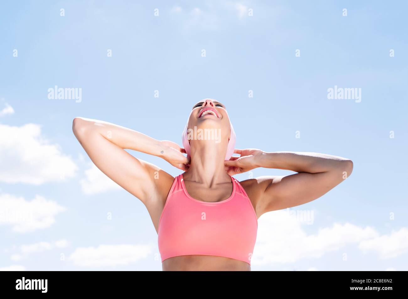 Alegre mujer deportiva con velo mientras se está de pie contra el cielo azul Foto de stock