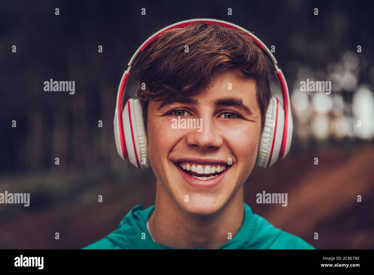 Adolescente con auriculares con impermeable en el bosque Foto de stock