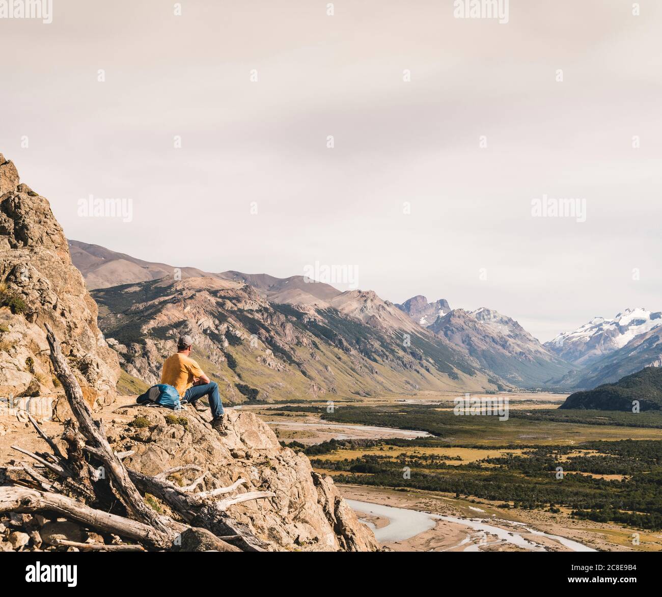 Hiker macho mirando a los Andes de la Patagonia contra el cielo mientras se sienta sobre el rock, Argentina Foto de stock