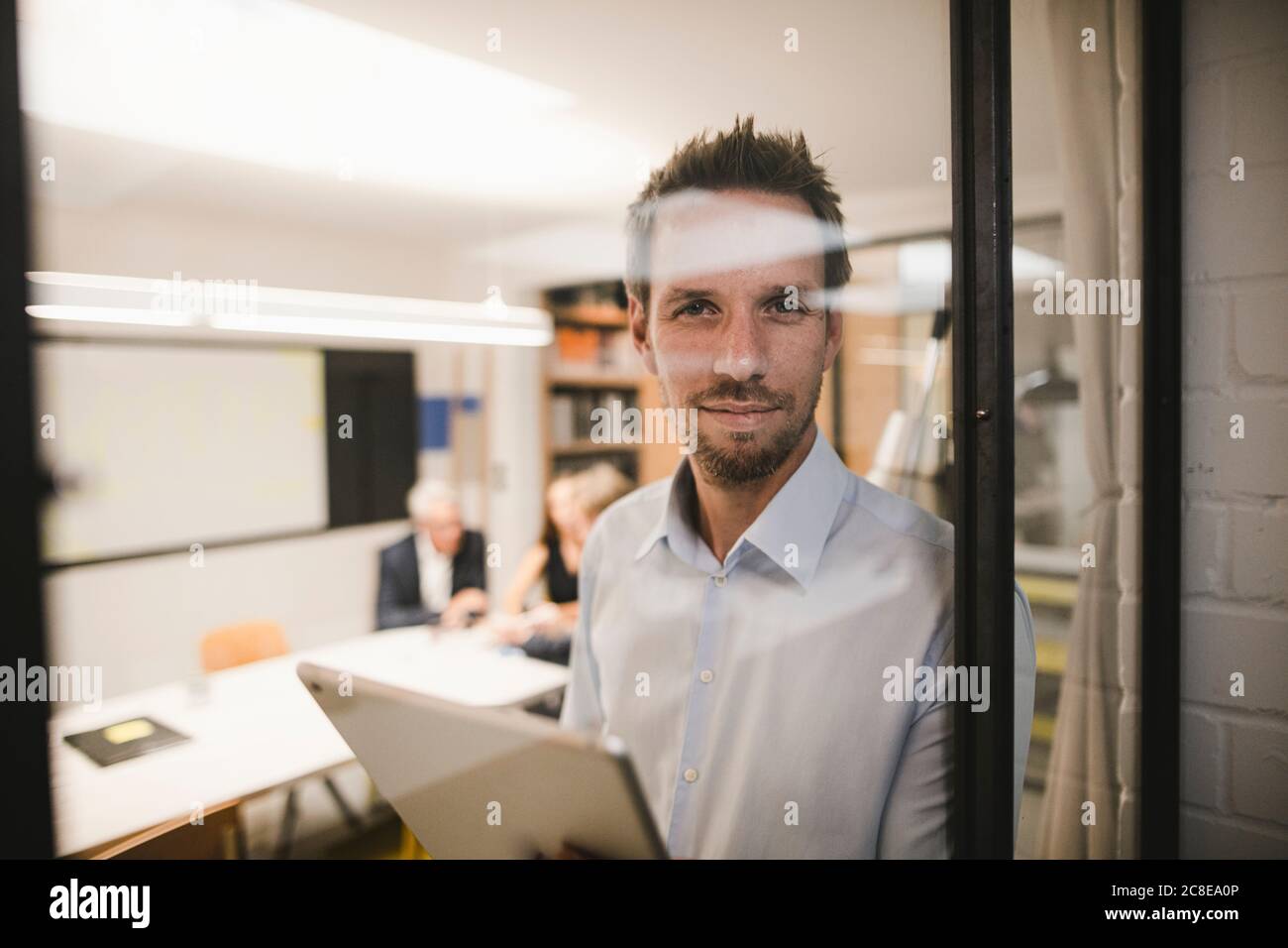 Hombre de negocios con tableta digital, mirando fuera de la ventana de la oficina Foto de stock