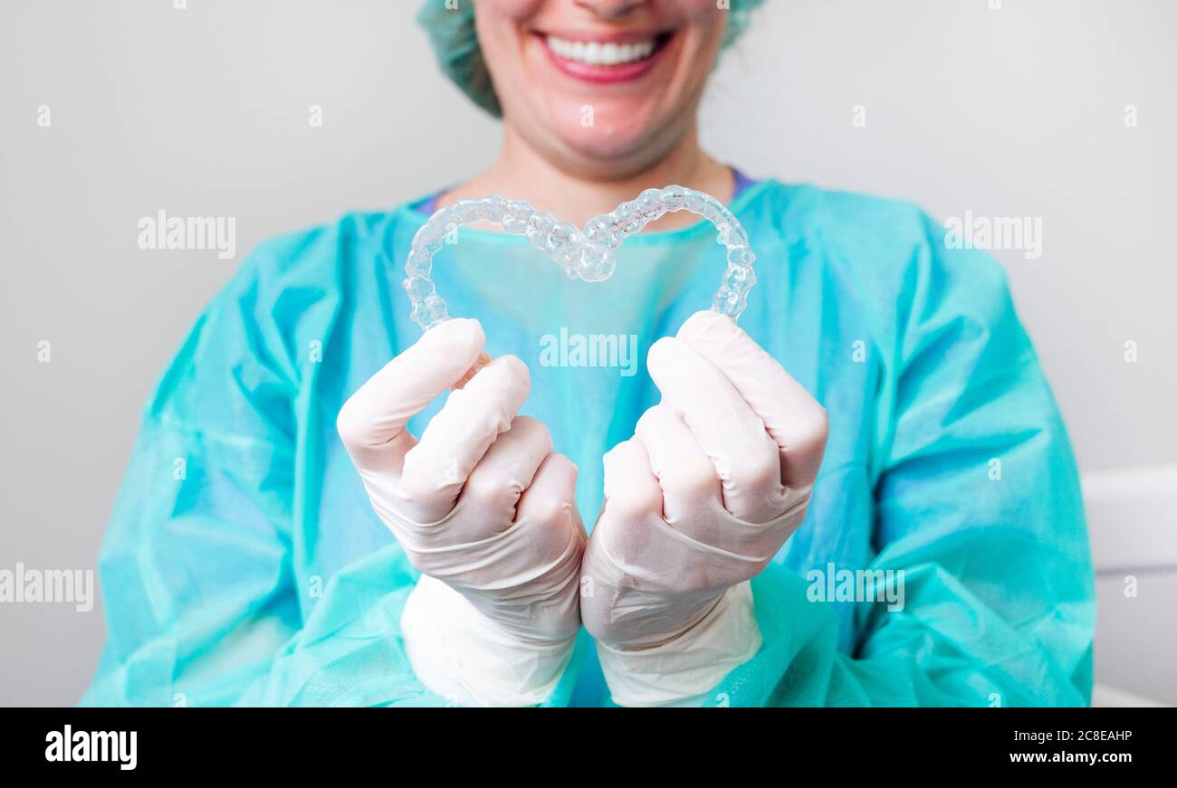 Primer plano de la enfermera que sostiene a los alineadores dentales en forma de corazón en clínica Foto de stock