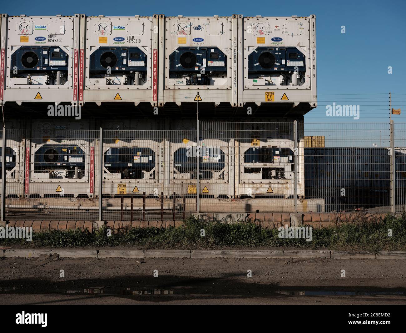 Apilados contenedores refrigerados blancos detrás de una valla eléctrica en una parte industrial de la ciudad. No hay gente. Foto de stock