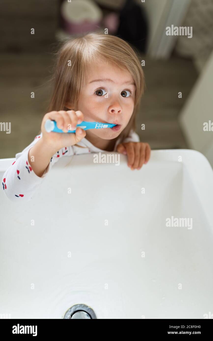 Niña en el cuarto de baño brillante cepillándose los dientes por encima del lavabo. Foto de stock