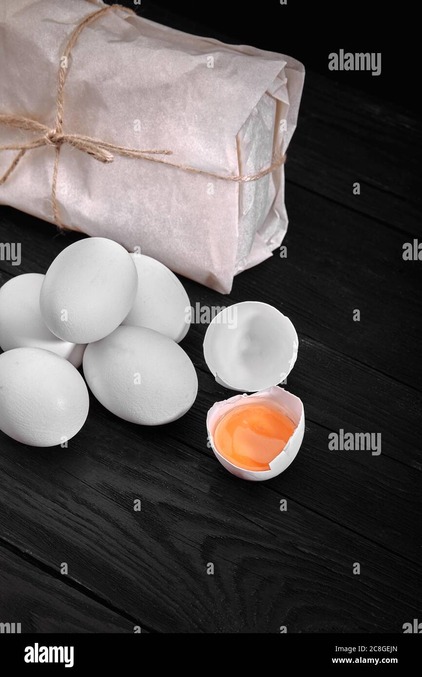 Huevos blancos de pollo frescos con heno en saco y madera rústica, agricultura orgánica sobre fondo negro. Alimentos naturales saludables Foto de stock