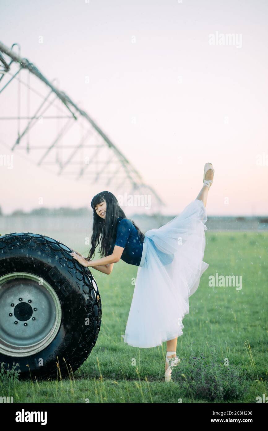 Bailarina japonesa en falda blanca se levanta y realiza la postura de la  golondrina en el campo en la granja cerca de la rueda de la pulverizadora  agrícola Fotografía de stock -