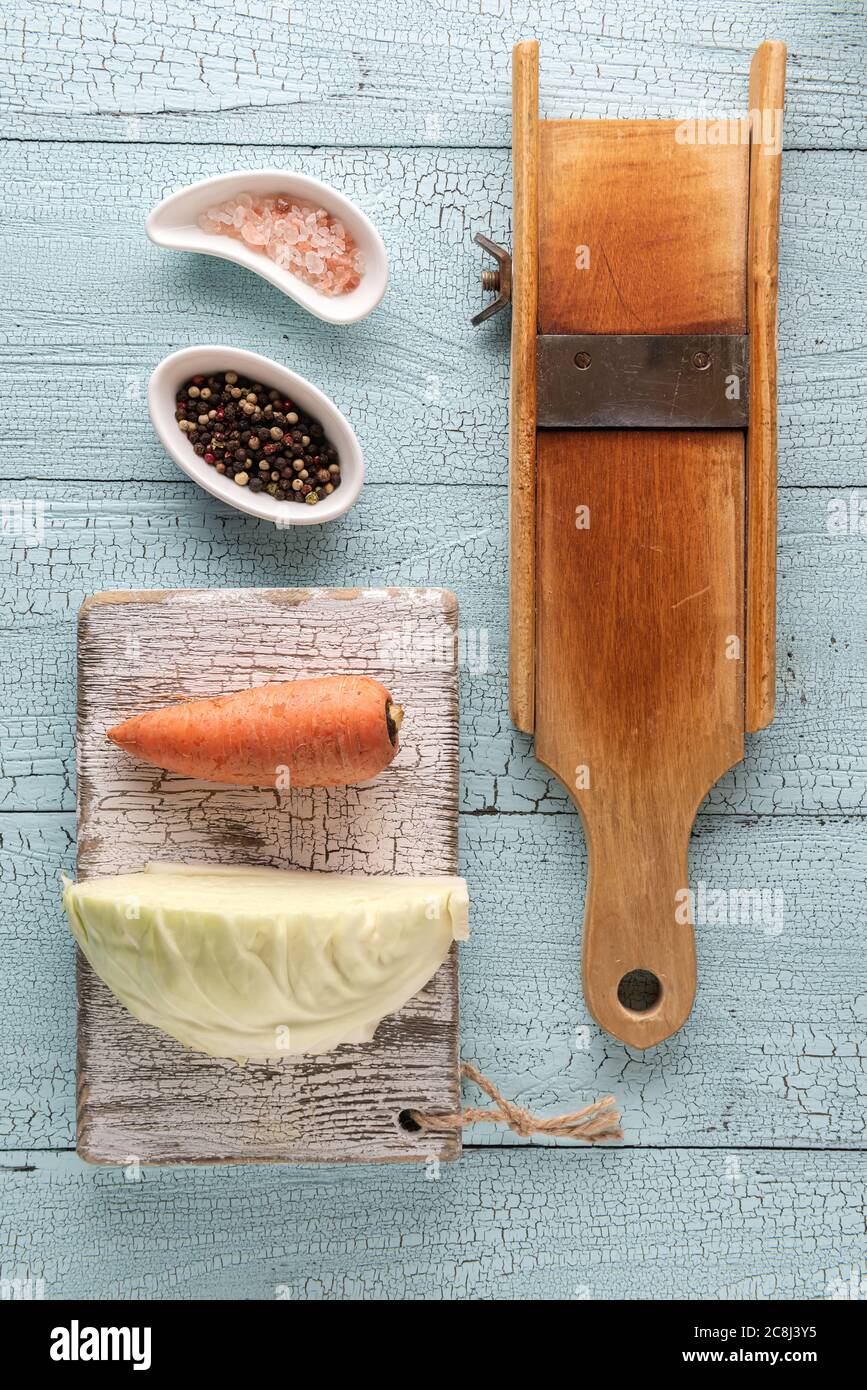 Repollo de madera rallador, pedazo de repollo, zanahoria, pimienta variada  y sal del himalaya en tabla de cortar y en la mesa de madera azul. Plano  con col f Fotografía de stock 