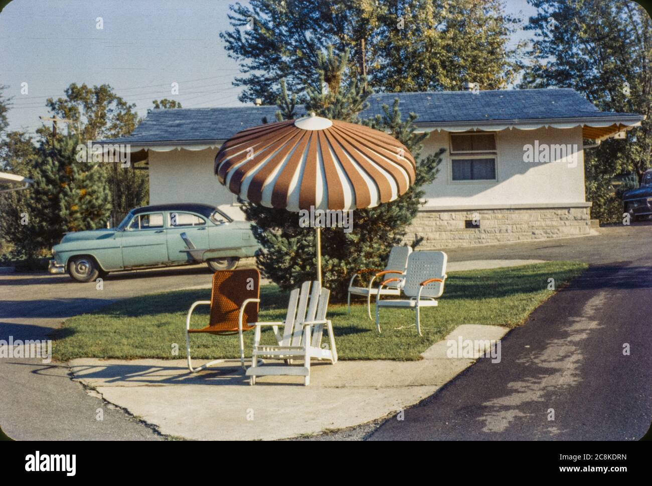 Coche estacionado en un motel al borde de la carretera con sillas y sombrillas al aire libre de mediados de siglo en Brown County, Indiana en la década de 1950. Foto de stock