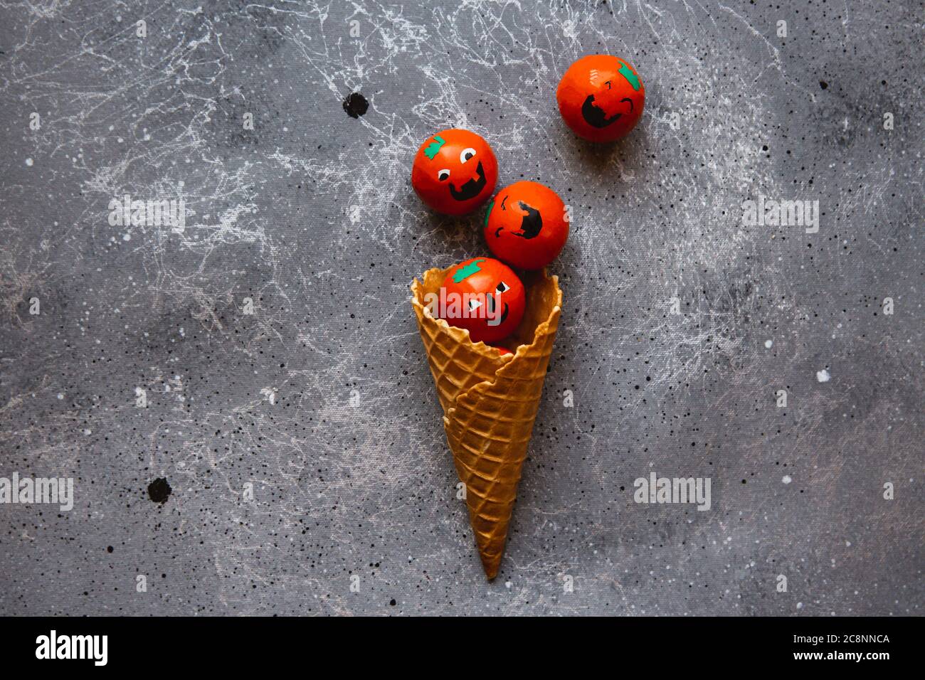 Cono de waffle está lleno de caramelos calabaza de Halloween sobre el fondo gris Foto de stock