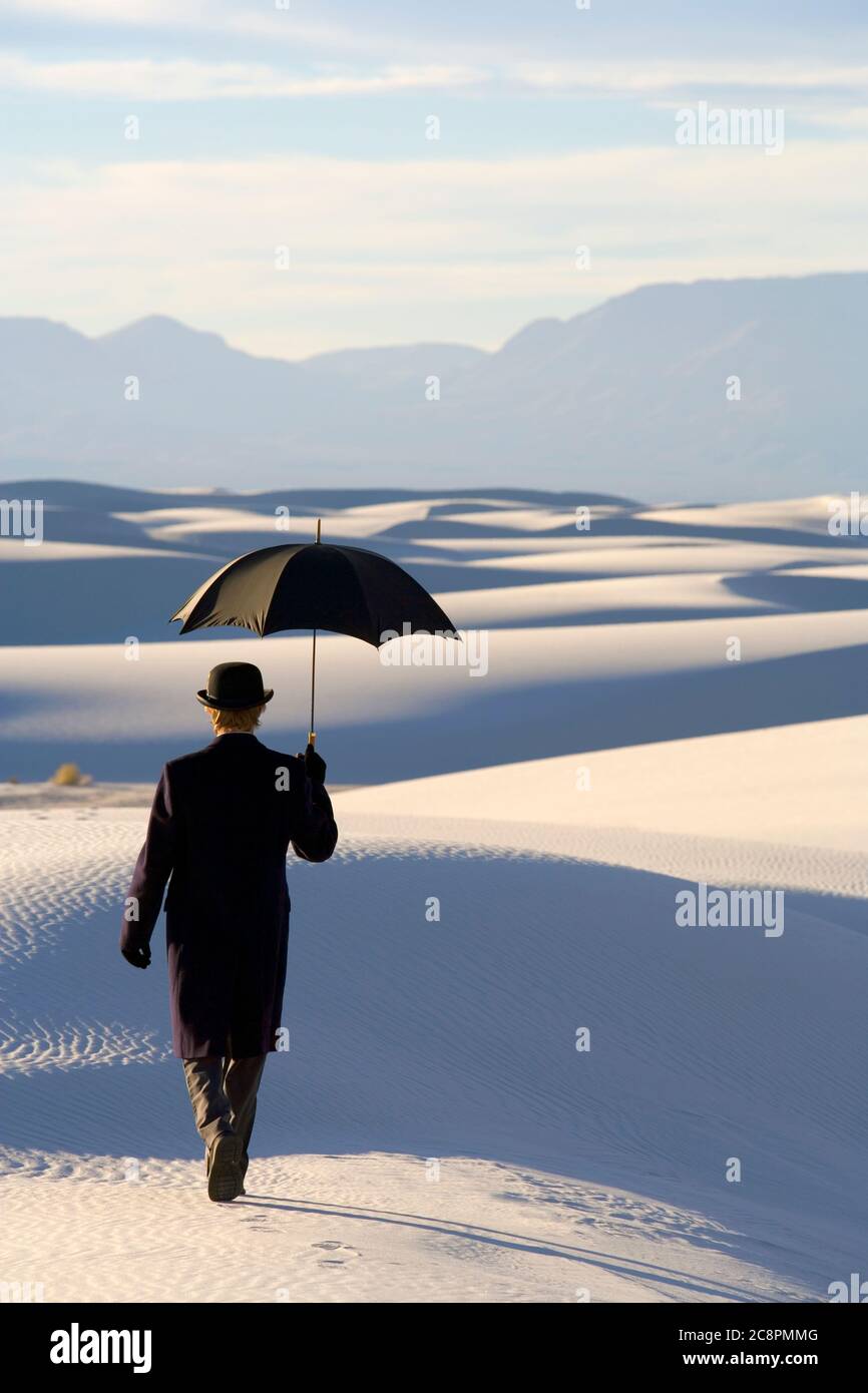 Hombre en un abrigo y traje negro, un sombrero de pajarita y paraguas, en  un desierto blanco desierto de arena blanca Fotografía de stock - Alamy