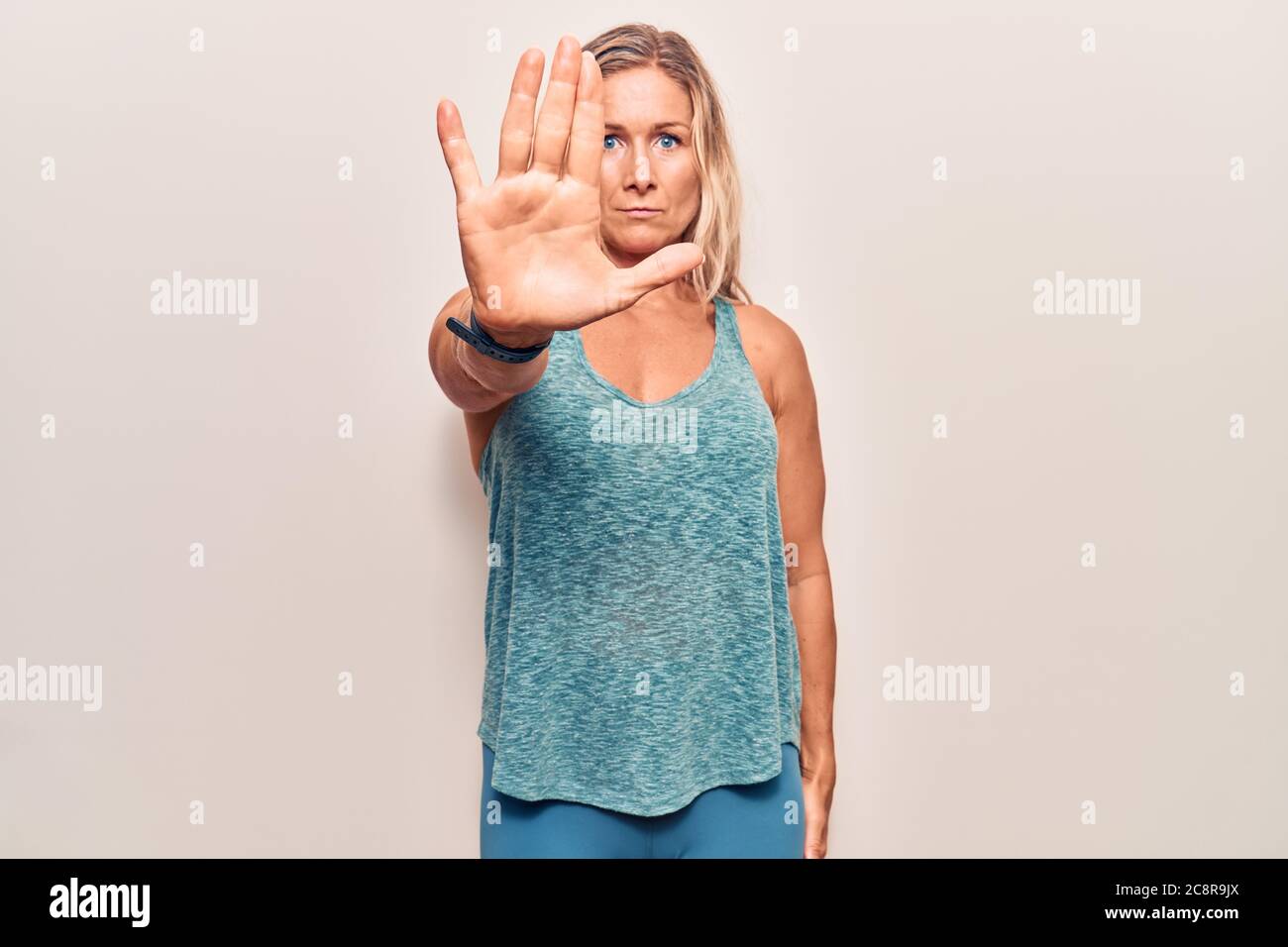 Edad media mujer rubia caucásica con ropa deportiva dejar de cantar con la  palma de la mano. Advertencia expresión con gesto negativo y serio en th  Fotografía de stock - Alamy