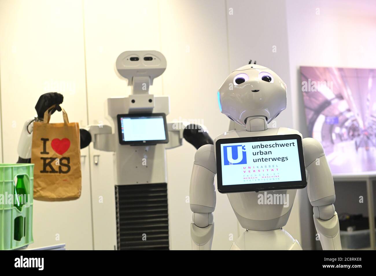 Kassel, Alemania. 14 de julio de 2020. Robot Pepper (r) se encuentra  delante de un robot de transporte con una bolsa en su mano. Los robots  forman parte del proyecto de investigación