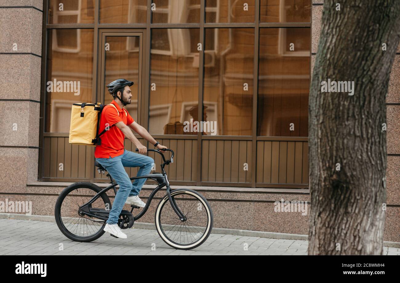 Entrega rápida en la ciudad. El joven con casco y mochila de entrega paseos en bicicleta Foto de stock