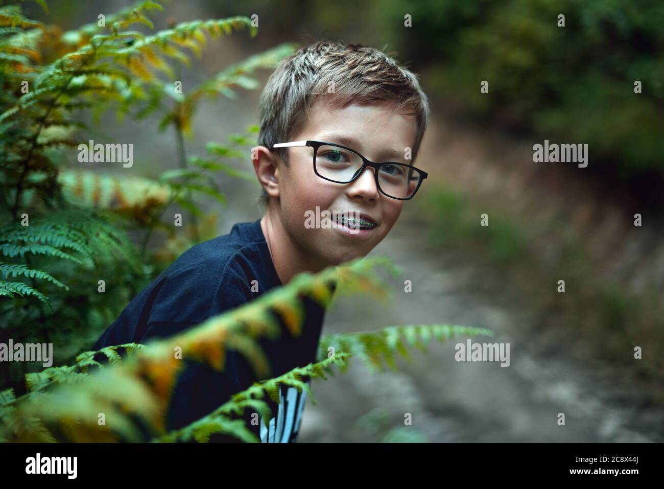 Retrato de un joven adolescente feliz jugando en el bosque, escondiéndose detrás del helecho. Foto de stock