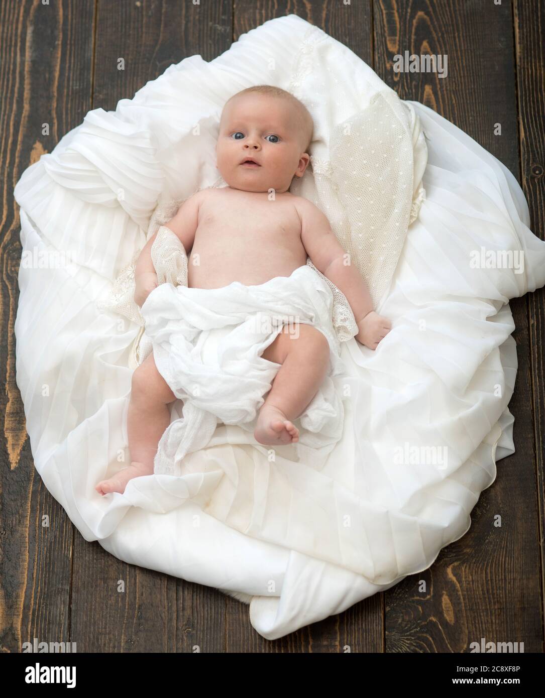Bebé cubierto con manta blanca. Concepto de infancia e inocencia. Bebé  tumbado sobre un suave edredón blanco diseñado como nube o nido. Niño recién  nacido con ojos azules y cara curiosa sobre