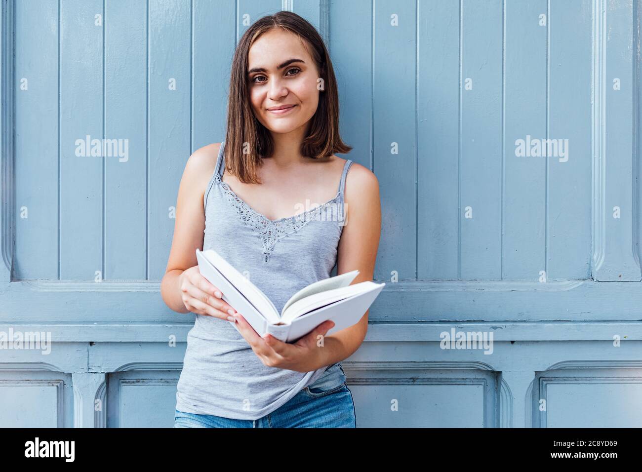 La niña sonríe y sostiene un papel blanco abierto gris azulado Foto de stock