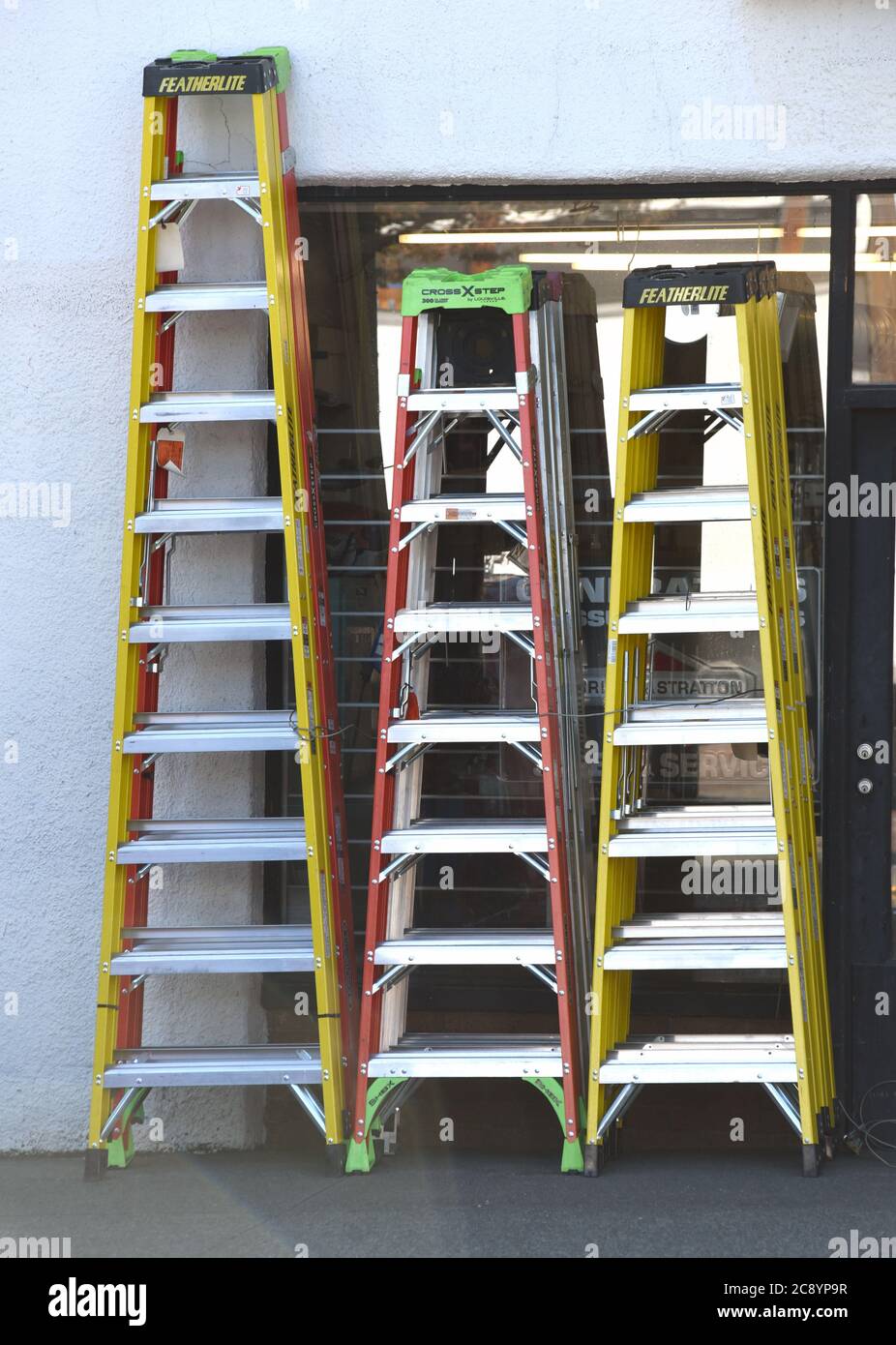 Escaleras de varias alturas se sientan en una acera fuera de una ferretería en Columbia Británica, Canadá. Foto de stock