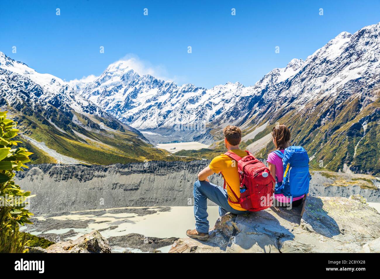Backpackers pareja de senderismo mirando Mount Cook vista en las montañas de pisotear en Nueva Zelanda. Gente excursionistas relajándose durante la caminata en los alpes de la isla del sur Foto de stock