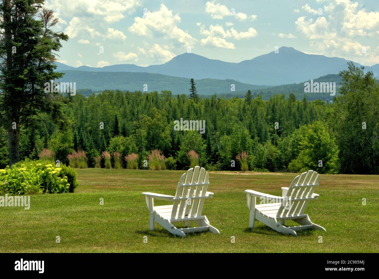 vista escénica tranquila, Whitefield, New Hampshire. Sillas blancas con vistas a la ladera de exuberantes árboles perennes enmarcados por montañas distantes. Foto de stock