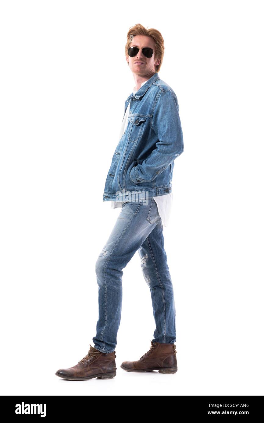 Vista lateral de joven jengibre macho modelo de moda en vaqueros chaqueta y botas de cuero. Cuerpo entero aislado sobre fondo blanco. Foto de stock