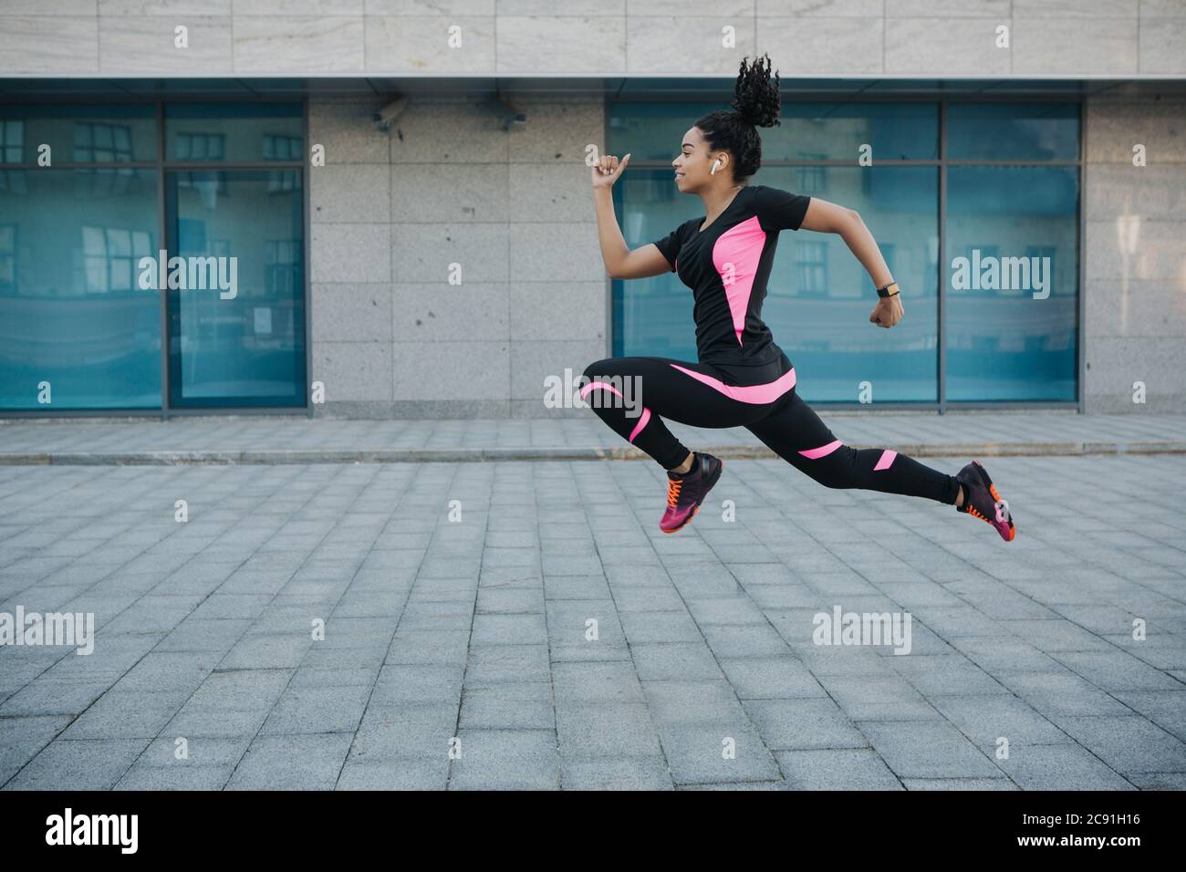 Ejercicio por pérdida de peso. Mujer en ropa deportiva con auriculares inalámbricos congelados en el aire, saltar mientras corres Foto de stock
