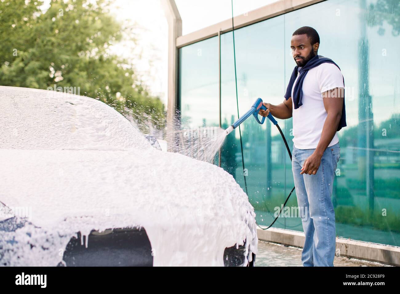 Limpieza al aire libre del coche con espuma de jabón usando chorro de alta  presión. Un joven africano guapo y barbudo lavando su coche moderno bajo  alta presión con Fotografía de stock 